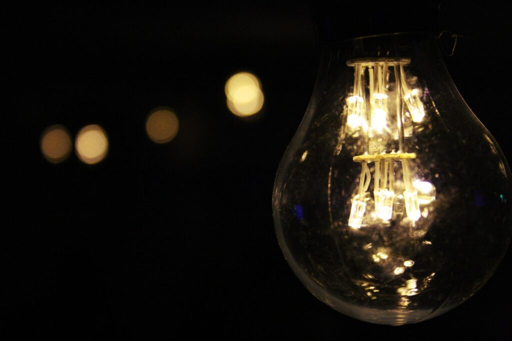 negócio de sucesso Em primeiro plano, há uma lâmpada acesa em um ambiente escuro. Ao fundo, fora de foco, há algumas outras lâmpadas também acesas.