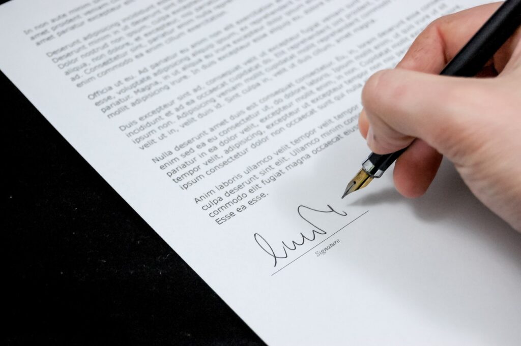 É possível ver a mão de uma pessoa segurando uma caneta e fazendo uma assinatura em um contrato. Problemas jurídicos que podem prejudicar sua empresa