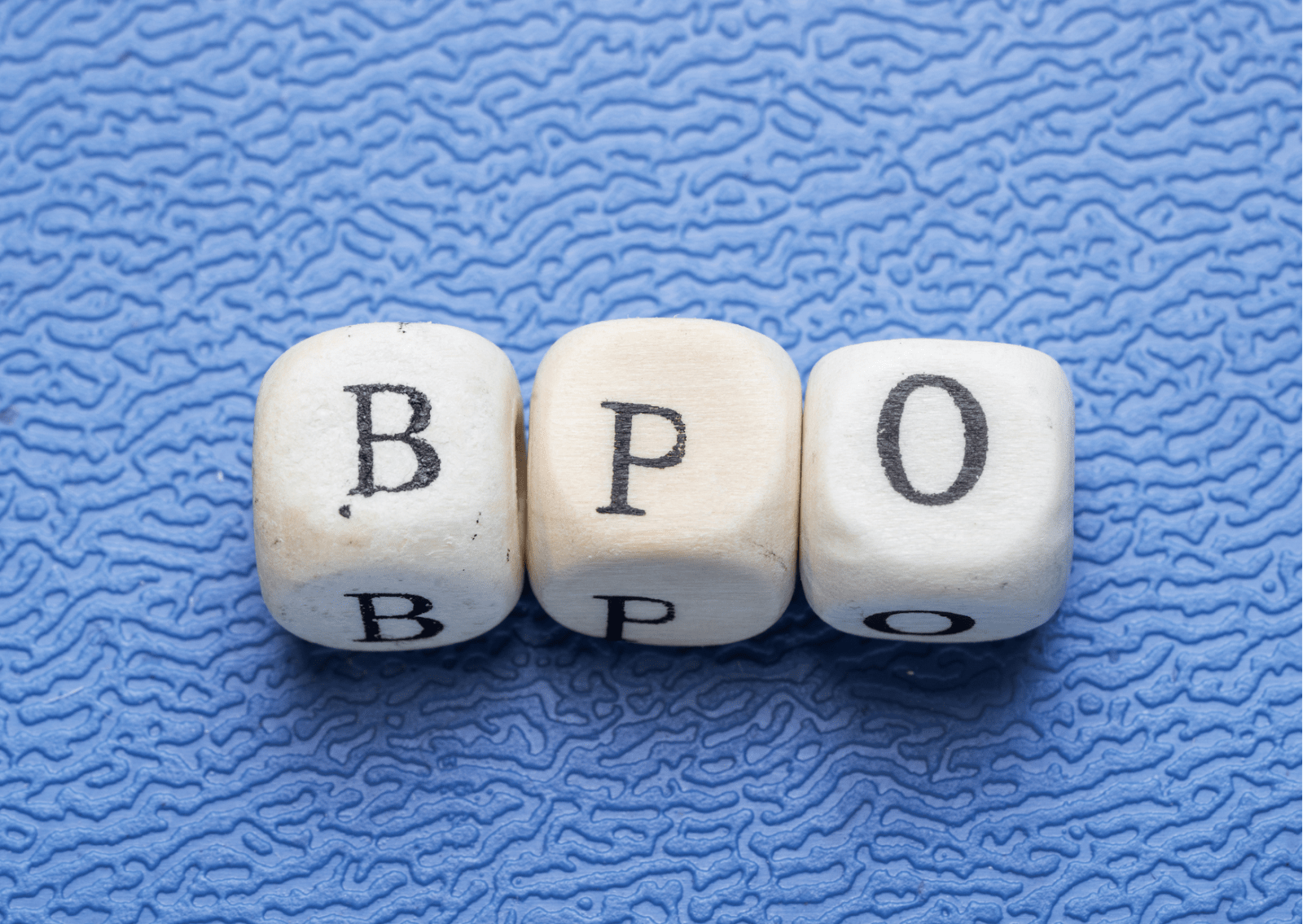 Em um fundo texturizado azul, vemos três dadinhos de letra, que formam a sigla BPO, em alusão à terceirização.