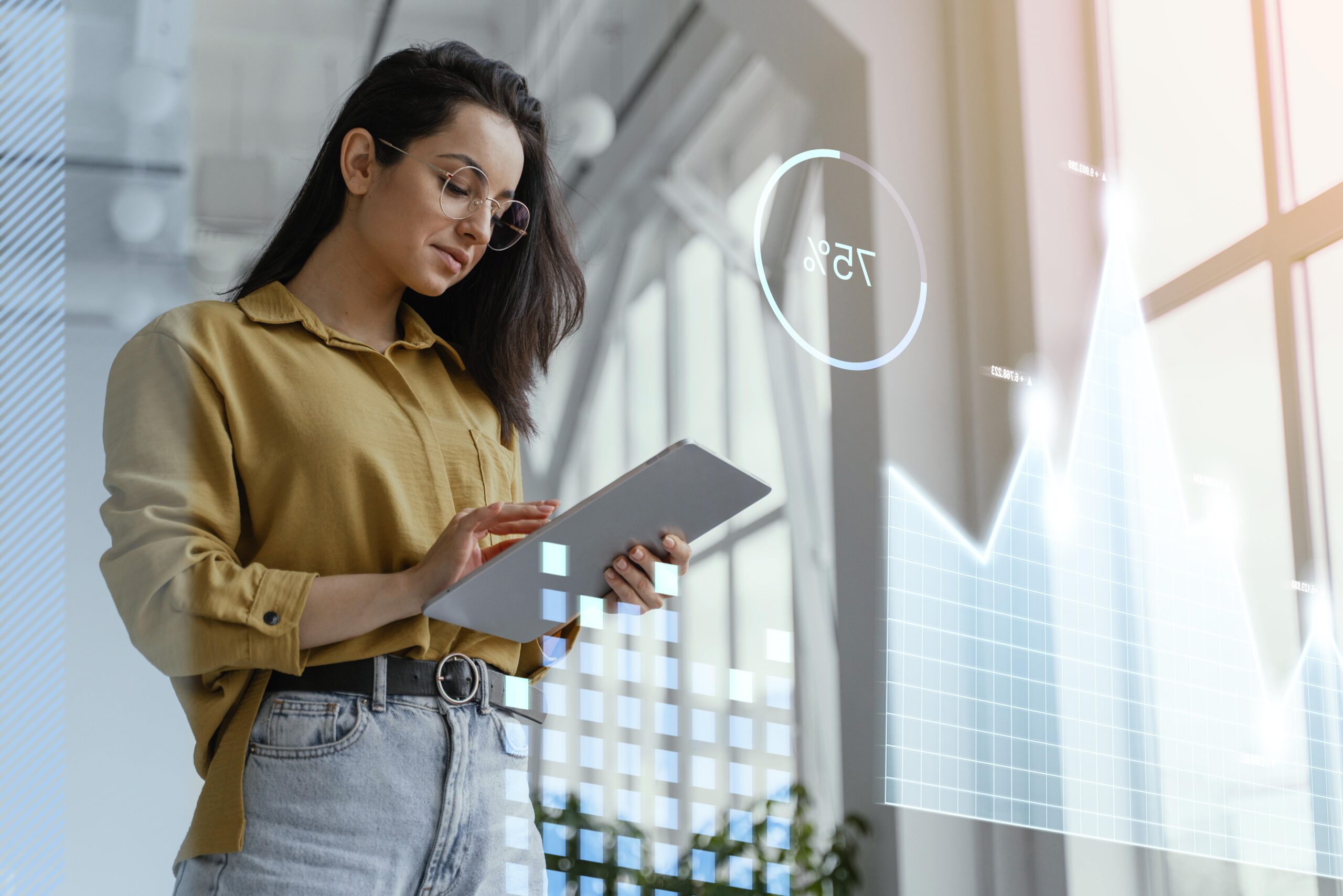 Jovem mulher em pé, vestindo camisa mostarda, calça jeans, cinto e óculos redondo, mexe em tablet com cara satisfeita. Em primeiro plano, como se fosse a tela do tablet, vemos gráficos e outros dados que simbolizam a contabilidade digital e os benefícios para empreendedores. 