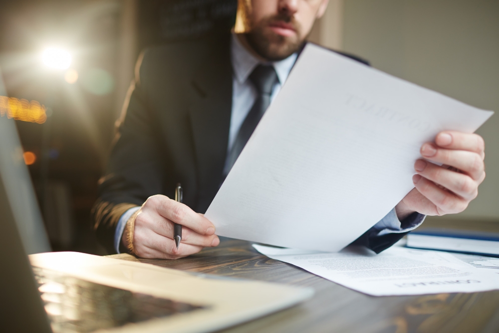 Empresário trabalhando com documentação na mesa para ilustrar assim artigo sobre como evitar multas e sanções fiscais com gestão contábil