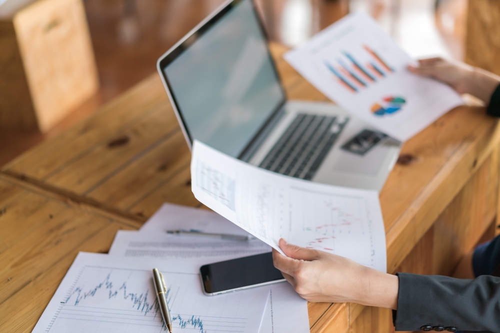 mulher de negócios com gráficos financeiros e laptop na mesa para ilustrar assim artigo sobre demonstrações contábeis.