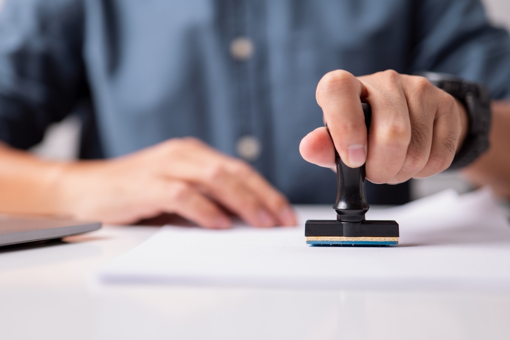 Foto close do carimbo de uma pessoa com a mão em um formulário de inscrição aprovado para ilustrar assim artigo sobre quanto custa o registro de marca no Brasil