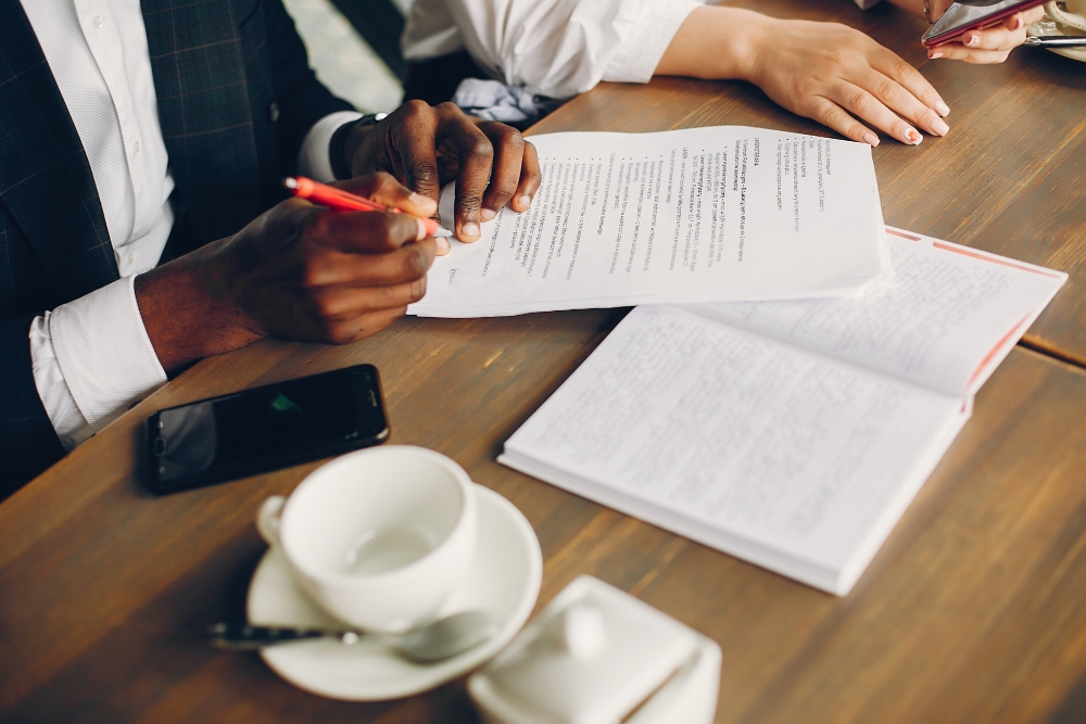 Foto de parceiros de negócios, sentados em um café, assinando documentos, para ilustrar assim artigo sobre terceirização de diligências de atos societários