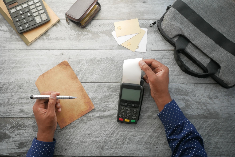 Vista superior da máquina pos e papel em rolo longo na mesa para ilustrar assim artigo sobre como simplificar os cálculos da folha de pagamento