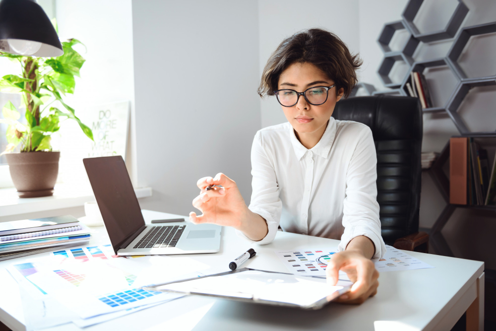 Foto jovem empresária sentada no local de trabalho no escritório, mexendo e analisando papéis, para ilustrar assim artigo sobre como começar o BPO Financeiro em seu escritório de contabilidade